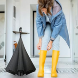 Woman in raincoat and wellies stands beside her black reverse umbrella, ready for rain