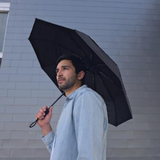 Man in blue button-down holds Repel windproof compact umbrella outdoors by a tiled building