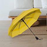 A best-selling yellow bright fun bold pop of color compact travel umbrella leans on its side in front a cream colored loveseat and jute rug. The room appears aesthetic, contrasting the umbrella.