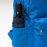 Navy compact umbrella tucked in a blue backpack’s side pocket, handle showing auto button and strap