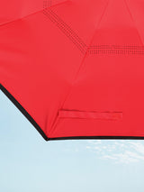 A zoomed in photo of a corner of a red umbrella canopy with black trim.