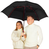 Smiling couple in matching white sweaters under a large black umbrella with red spokes.